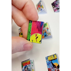 May include: Miniature comic books, including a "Watchmen" comic held in a hand. Other comics visible include "Hulk" and "Iron Man". The "Watchmen" comic has a yellow and red cover with the word "Watchmen" in green.