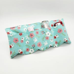 May include: A floral print makeup organizer in a light blue fabric. The organizer has multiple pockets holding various cosmetic items. The fabric features a pattern of pink and white flowers with green leaves. The edges have a scalloped design.