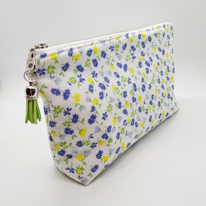 May include: A white zippered pouch with a green tassel. The pouch is covered in a small blue and yellow floral pattern.