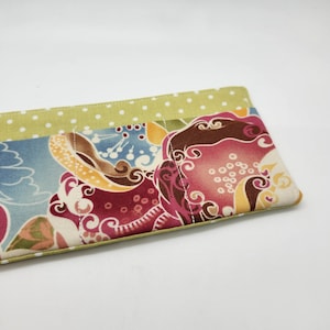 May include: A rectangular fabric item with a floral pattern in shades of blue, red, and yellow. The top edge is a light green with white polka dots. The item appears to be quilted with visible stitching.