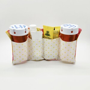 May include: A fabric organizer with three pockets, holding two prescription bottles and small toiletries. The pockets are made of white fabric with yellow polka dots. The Naked Bee product is visible.