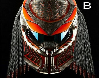 Può includere: Un casco da moto nero e arancione con un design ispirato al Predator. Il casco ha una visiera nera e una vernice nera e arancione con un motivo tribale. Il casco ha anche una serie di dreadlocks neri attaccati alla parte posteriore.