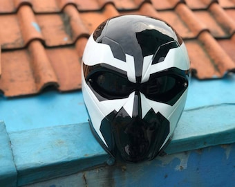 May include: A black and white motorcycle helmet with a skull-like design. The helmet has a clear visor and a black chin strap.