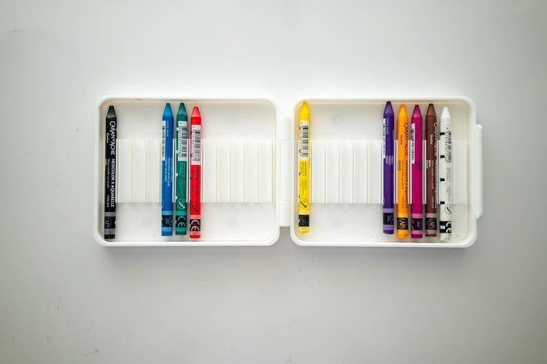 Peut inclure: Un &eacute;tui en plastique blanc contenant un jeu de 10 crayons de couleur. Les crayons sont dispos&eacute;s en deux rang&eacute;es de cinq. Les crayons sont noir, bleu, vert, rouge, jaune, violet, orange, rose, marron et blanc.