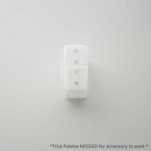 May include: A white, rectangular accessory with a textured surface, featuring two stacked sections, each with three small, silver-colored dots. The accessory has a small, rectangular attachment on the side. The text "*Trick Palette NEEDED for accessory to work *" is at the bottom.