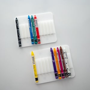 Peut inclure: Deux supports en plastique blanc avec des rang&eacute;es de fentes pour ranger des crayons. Le support du haut contient un crayon noir et cinq crayons de couleur&nbsp;: bleu, vert, bleu clair, rouge et orange. Le support du bas contient six crayons de couleur&nbsp;: jaune, violet, orange, rose, marron et blanc.