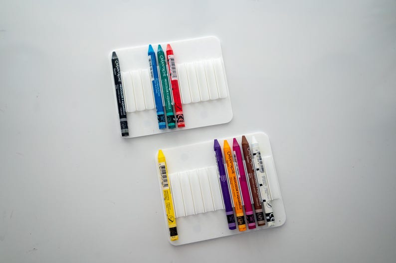 Peut inclure: Deux supports en plastique blanc avec des rang&eacute;es de fentes pour ranger des crayons. Le support du haut contient un crayon noir et cinq crayons de couleur&nbsp;: bleu, vert, bleu clair, rouge et orange. Le support du bas contient six crayons de couleur&nbsp;: jaune, violet, orange, rose, marron et blanc.