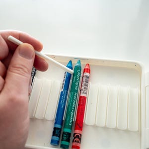 Peut inclure: Gros plan sur un jeu de crayons aquarelle dans un &eacute;tui blanc. Les crayons sont bleu, vert, rouge et jaune. Un coton-tige blanc est utilis&eacute; pour m&eacute;langer les couleurs.