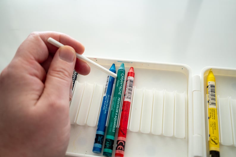 Peut inclure: Gros plan sur un jeu de crayons aquarelle dans un &eacute;tui blanc. Les crayons sont bleu, vert, rouge et jaune. Un coton-tige blanc est utilis&eacute; pour m&eacute;langer les couleurs.