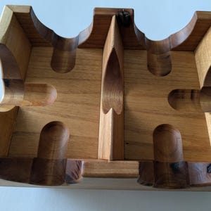 May include: A handcrafted wooden pipe stand with a natural finish. The stand features multiple curved slots and rounded holders, designed to securely hold pipes. The wood grain is visible, adding to the rustic aesthetic.