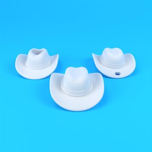 May include: Three small, solid white cowboy hats arranged in a triangular formation. Each hat features a classic pinched crown and a wide, curved brim. One of the hats on the right side includes a small, circular hole punched through the brim.