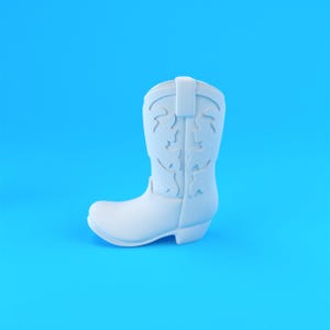 Op de afbeelding: Een effen wit cowboylaarsfiguurtje met een klassieke hoge schacht met decoratieve uitgesneden patronen aan de zijkanten, een ronde neus en een lage blokhak, gepresenteerd tegen een levendige, effen felblauwe achtergrond.