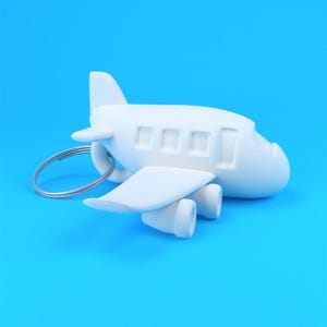 Könnte beinhalten: Ein mattweißer Flugzeug-Schlüsselanhänger mit einem stilisierten, abgerundeten Rumpf, drei quadratischen Fenstern und zwei unter den Flügeln montierten Triebwerken. Ein silberner Metallring ist an der Rückseite des Flugzeugkörpers befestigt.