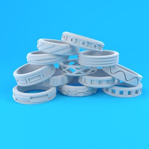 Pode incluir: Um monte de anéis de silicone branco com diferentes padrões e designs. Os anéis estão empilhados uns sobre os outros e estão dispostos em uma ordem aleatória.
