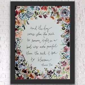 May include: A framed watercolour print with a floral border in pinks, blues, and purples. The artwork displays handwritten text: "And the day came when the risk to remain tight in a bud was more painful than the risk it took to blossom." Signed "Anaïs Nin."