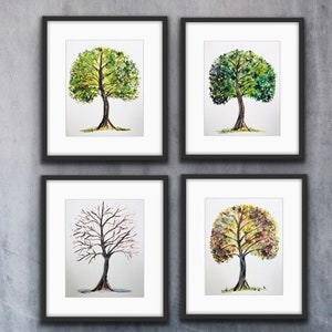 May include: Four framed watercolour paintings of a tree in different seasons. The top left painting shows a tree with green leaves, the top right painting shows a tree with green leaves, the bottom left painting shows a tree with bare branches, and the bottom right painting shows a tree with yellow and orange leaves.