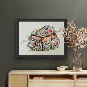 Peut inclure: Une peinture &agrave; l'aquarelle d'un piano &agrave; queue avec des fleurs qui poussent dessus. Le piano est brun et les fleurs sont roses, violettes et jaunes. La peinture est encadr&eacute;e en noir.