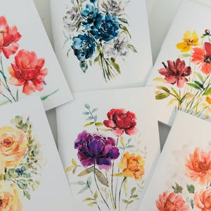 Peut inclure: Une collection d'estampes d'art floral à l'aquarelle présentant diverses fleurs dans des tons de rouge, orange, jaune, bleu et violet. Chaque estampe présente un bouquet unique de fleurs avec un feuillage vert sur fond blanc.