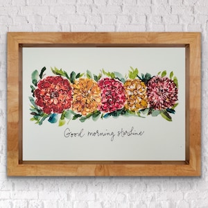 May include: A watercolor painting of a row of five orange, red, and yellow flowers with green leaves. The text "Good morning sunshine" is written below the flowers.