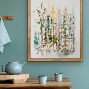 May include: A framed watercolor painting of a forest scene with trees in shades of green, brown, and pink. The painting is set against a light green wall.