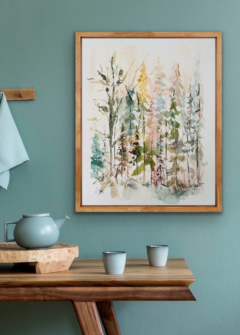 May include: A framed watercolor painting of a forest scene with trees in shades of green, brown, and pink. The painting is set against a light green wall.