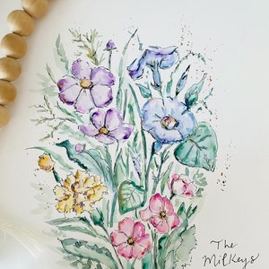 May include: Watercolor painting of a bouquet of flowers in shades of purple, blue, pink, and yellow. The flowers are surrounded by green leaves and stems. The painting is signed "Sarah O'Neil" in the bottom left corner and includes the text "The Milkeys Est. 2020" in the bottom right corner.