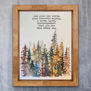 Puede incluir: Una impresión en acuarela enmarcada con una escena de bosque en tonos verdes, marrones y azules. La obra de arte incluye el texto: "Agrega tus propias palabras, tu frase favorita, una cita, una letra, un estímulo que puedas leer todos los días."