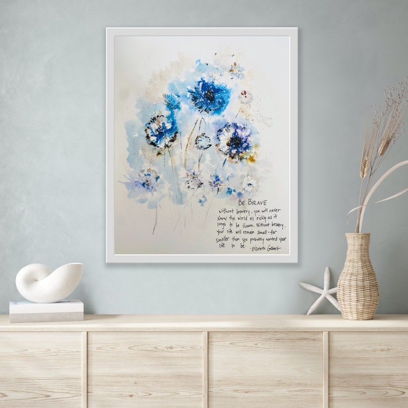May include: A framed watercolor painting of blue flowers with a white background. The quote "BE BRAVE without bravery, you will never know the world as richly as it longs to be known. Without bravery, your life will remain small-for smaller than you probably wanted your life to be. - Elisabeth Gilbert" is written in black ink below the flowers.