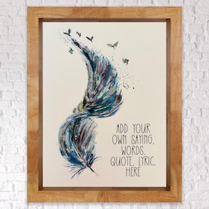 May include: A framed print featuring a watercolour-style feather in shades of blue, purple, and black, with small birds flying upwards. The text reads: ADD YOUR OWN SAYING, WORDS, QUOTE, LYRIC, HERE. The artwork is enclosed in a light brown wooden frame.