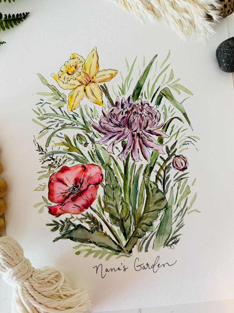 May include: Watercolor painting of a bouquet of flowers, including a yellow daffodil, a pink chrysanthemum, and a red poppy. The flowers are surrounded by green leaves and stems. The painting is signed "Nana's Garden" in the bottom right corner.