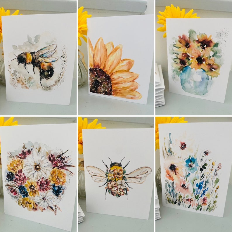 Puede incluir: Una colecci&oacute;n de tarjetas de felicitaci&oacute;n en acuarela con dise&ntilde;os florales e insectos. Las tarjetas muestran un abejorro, girasoles y varios arreglos florales en tonos amarillos, naranjas, azules y blancos. Cada tarjeta se muestra sobre un fondo blanco.