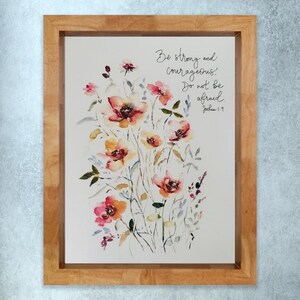 May include: Framed watercolour floral print. The artwork shows a bouquet of pink, orange, and yellow flowers with green leaves. The text reads "Be strong and courageous! Do not be afraid Joshua 1:9.", in a light brown wooden frame.
