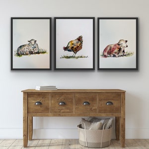 May include: Three framed watercolour paintings of farm animals. The paintings are of a sheep, a hen, and a calf. The paintings are all in a similar style, with a white background and a light wash of colour.