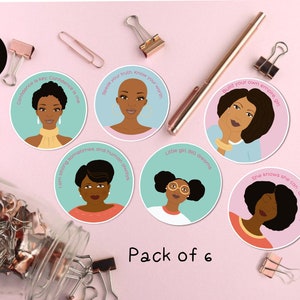 Op de afbeelding: Een set van zes ronde stickers met illustraties van zwarte vrouwen met inspirerende boodschappen. De stickers zijn op een roze achtergrond met gouden paperclips en een pen.