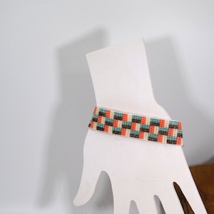 May include: A beaded bracelet featuring a geometric pattern in shades of brown, orange, white, and teal.