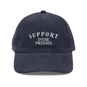 Peut inclure: Casquette de baseball en velours côtelé bleu marine avec l'inscription blanche brodée "SUPPORT INDIE PRESSES". La casquette a une visière incurvée et une sangle réglable. Un accessoire décontracté classique.