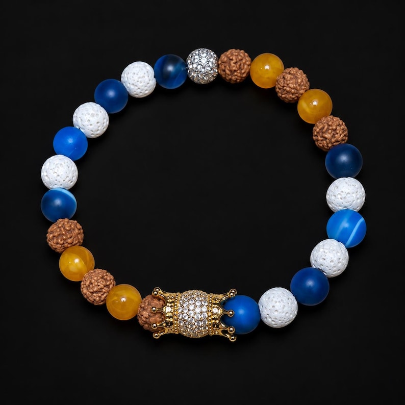 Pu&ograve; includere: Un braccialetto di perline con un mix di perline blu, bianche, gialle e marroni testurizzate. Il design include sfere blu lisce, perline di lava bianche porose, perline gialle traslucide e semi di rudraksha marroni con una perlina a corona.