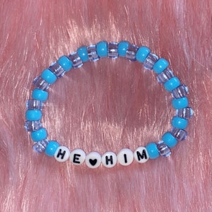 May include: A blue and clear beaded bracelet with the words "HE &hearts; HIM" spelled out in white beads.