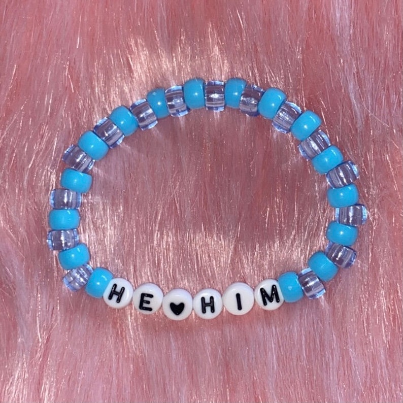 May include: A blue and clear beaded bracelet with the words "HE &hearts; HIM" spelled out in white beads.
