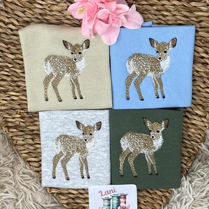 May include: Four embroidered deer designs on different colored squares: beige, light blue, gray, and dark green. A small square with the text "Lani Embroidery" and images of spools of thread is at the bottom. A pink flower is at the top.