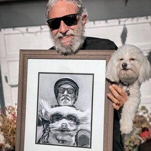 May include: A framed black and white pencil drawing of a man and a dog wearing sunglasses. The man is wearing a hat and the dog is wearing goggles. The drawing is in a brown frame.