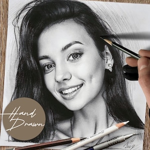 May include: A detailed pencil drawing of a smiling person with long dark hair. The drawing is in black and white, with shading to create depth and dimension. The words "Hand Drawn" are in a circle in the lower left corner. Pencils are in the foreground.