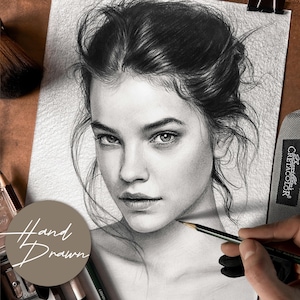 May include: A detailed pencil drawing of a woman's face, showcasing realistic shading and fine lines. The artwork is held with a clip, and the words "Hand Drawn" are visible. A makeup brush and pencils are in the background.