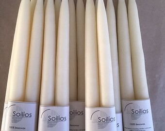 May include: A bundle of 10 long, tapered, off-white beeswax candles with white string wicks. The candles are packaged in clear plastic and have labels that read "Soilíos 100% Beeswax" with contact information.