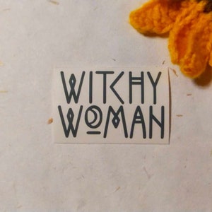 May include: A white sticker with the text "Witchy Woman" in black outlined letters.