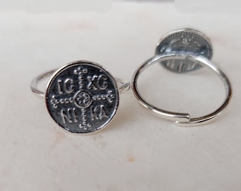 May include: A silver ring with a round, engraved design featuring a cross and the text "IC XC NIKA".
