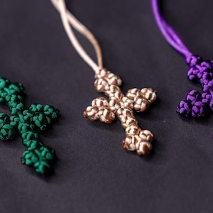 May include: Four knotted cross pendants in black, green, beige, and purple hanging from cords.