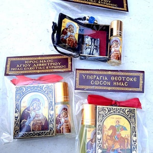May include: Several religious items are packaged in clear plastic bags. The items include small bottles with gold caps, religious icons, and small pouches. Text in Greek is visible on the packaging.