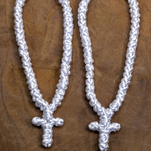 May include: Two white knotted prayer ropes with crosses at the end. One rope has a blue bead and the other has a red bead. The ropes are on a brown wooden surface.