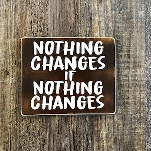 May include: A brown wooden sign with white text that reads "Nothing Changes If Nothing Changes".